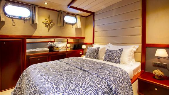 Comfortable bedroom on the sailing yacht with nautical decor and two porthole windows.