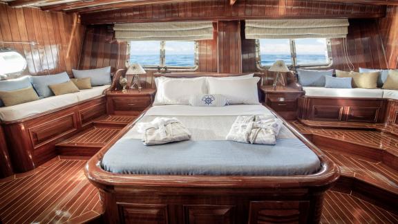 Luxurious cabin on the gulet Entre Cielos with a large bed, two seating areas and elegant wooden furnishings.