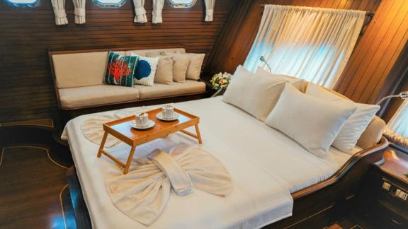 A cosy bedroom on a sailing ship, with a beautifully prepared bed and a breakfast tray with coffee.