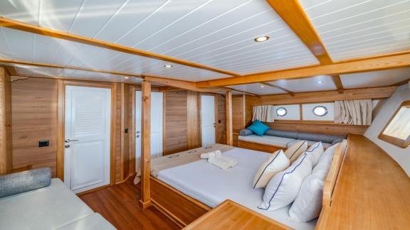 Ein geräumiges Schlafzimmer auf der Gulet-Yacht Amazon Solo mit Doppelbett, Holzmöbeln und gemütlicher Sitzecke.