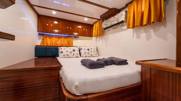 Second guest cabin of Gulet Lycian Sirius featuring a double bed, wooden furniture, and orange curtains.