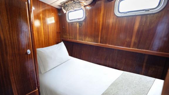 Compact cabin of Gulet Lina 2 with a single bed, wooden furniture, and two porthole windows.