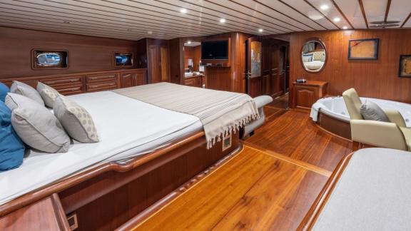 Luxurious bedroom on a boat with double bed, jacuzzi, sofa and wooden interior.