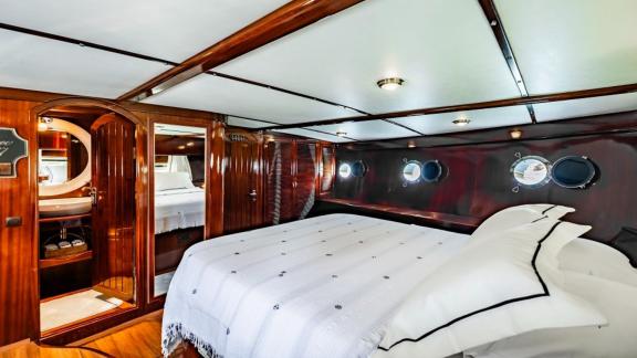 Master cabin with a large bed, portholes, and ensuite bathroom on Gulet Golden Joy in Bodrum.