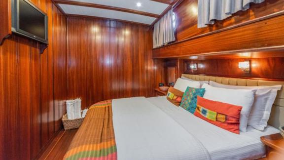 An elegant cabin on a 6-cabin gulet in Bodrum with a double bed, wooden walls and colourful cushions.