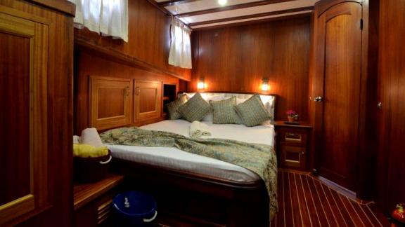 Cosy bedroom of the Gulet Smyrna with elegant wooden furnishings and soft bed.