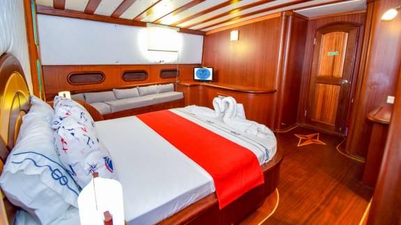 Elegante Kabine auf einer Segelyacht mit einem großen Bett, einer Sitzecke und warmen Holzmöbeln.