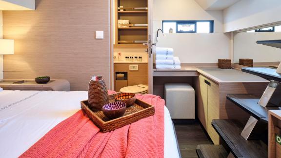 Cabin on the catamaran with a double bed, view of the ensuite bathroom, and a coral blanket.