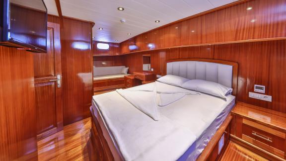 A spacious cabin on the Gulet Kasapoglu 6 featuring a double bed, sofa, and wood furnishings.