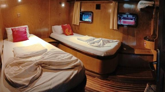 Cabin with two single beds, wooden walls, reading lamps, and windows with curtains on Gulet Nirvana 2.