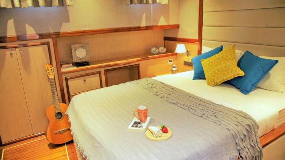 Comfortable bedroom on the sailing yacht with a guitar, stylish cushions, and breakfast tray.