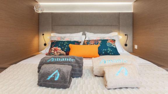 Stylish bed on a catamaran, decorated with colorful pillows and personalized towels.