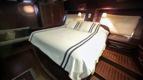 A luxurious cabin on board the Gulet Dulcinea with a large, cosy bed and stylish wood panelling.