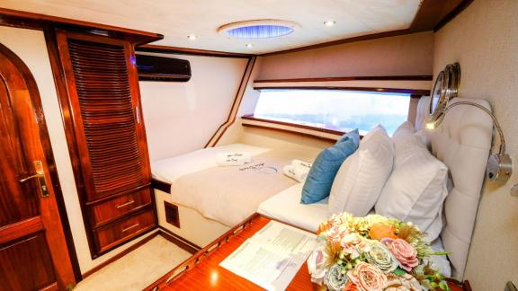 A cosy cabin on a yacht with a double bed, wooden furniture and a large window.