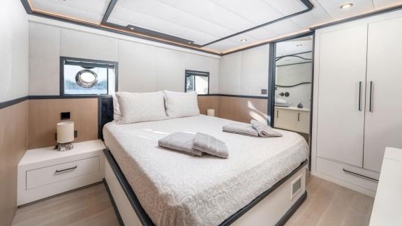 Modernly decorated yacht bedroom; offers a comfortable bed, nightstand, and wardrobe for a simple and elegant space.