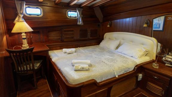 astefully furnished cabin of the Serenad yacht with a double bed, desk, and classic wood decor.