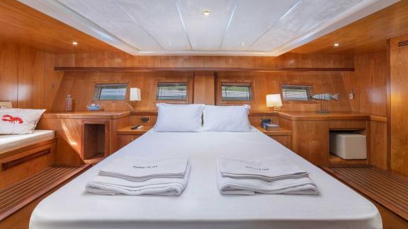 The main cabin of a Bodrum Gulet, equipped with a large double bed, wood panelling and warm light.