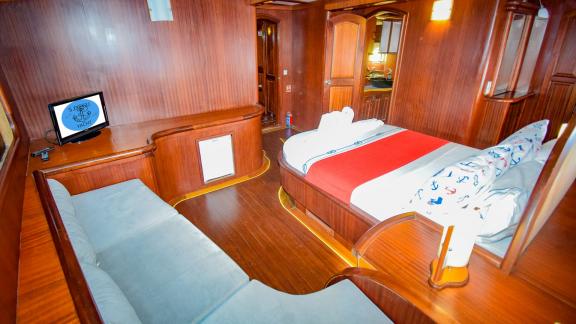 Cabin on a sailing yacht with a large bed, a seating area and elegant wooden furniture.