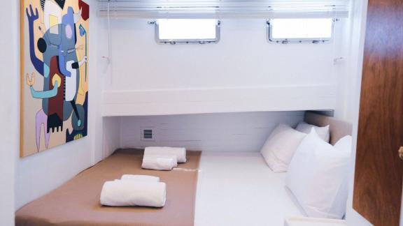 A simple, white bedroom with a double bed, towels and a colourful work of art on the wall.