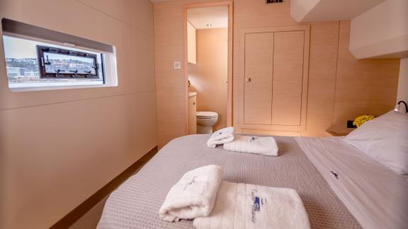 Stylish catamaran cabin with a large bed, window, and direct access to a modern bathroom.