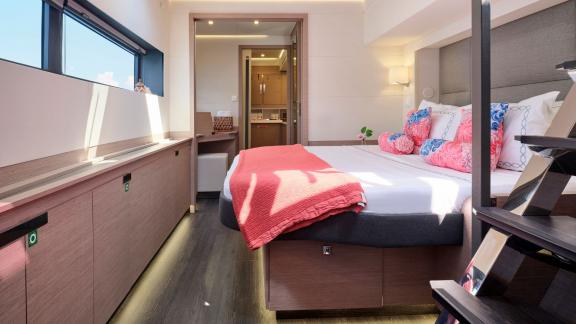 Spacious cabin on the catamaran with a double bed, coral blanket, and ensuite bathroom.