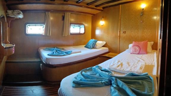 Cabin with two single beds, wooden walls, reading lamps, windows with curtains, and towels on Gulet Nirvana 2.