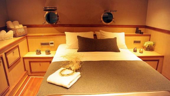 Stylish bedroom on the sailing yacht with two porthole windows and elegant decor.