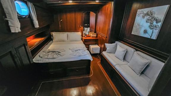 A cosy cabin on a sailing ship with a comfortable bed, sofa and wooden furnishings, perfect for relaxing at sea.