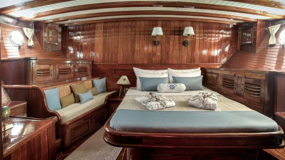 Luxurious cabin on the gulet Entre Cielos with fine wooden furnishings, large bed and cosy seating area.