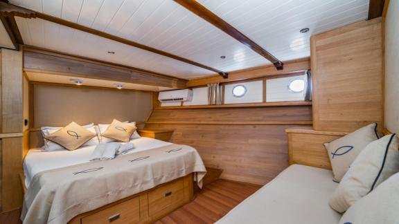 A cosy bedroom on the gulet yacht Amazon Solo with double bed and sofa, surrounded by wooden furniture.