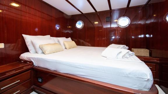 Cosy sleeping cabin in the Gulet Vivere with large bed, elegant wooden furnishings and small portholes.