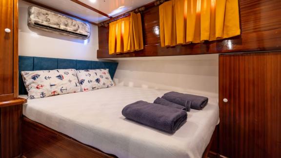 Fourth guest cabin of Gulet Lycian Sirius featuring a double bed, wooden furniture, orange curtains, and air conditionin