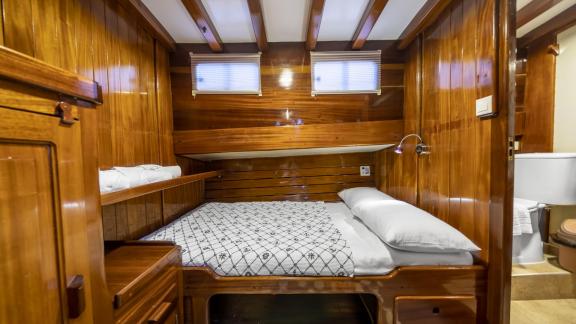 The double cabin features a bed with a patterned cover, wooden walls, storage, and an adjacent bathroom.