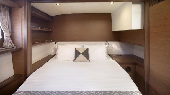 The cozy cabin of the Lagoon 560 in Athens features a welcoming double bed, shelves for storage, and warm lighting.