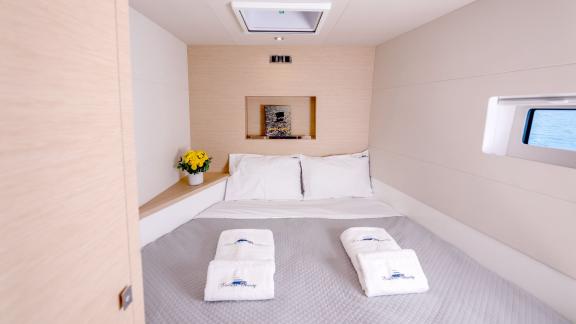 Inviting cabin on a catamaran featuring a large bed, side window, and skylight for natural lighting.