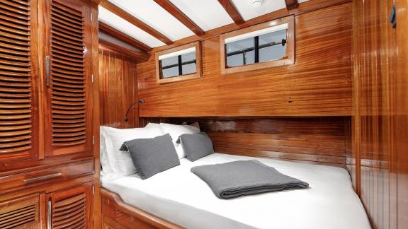 Wood-paneled cabin with a comfortable bed and two windows on Serenad A.