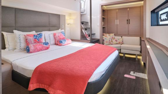 Spacious cabin on the catamaran with a double bed, coral blanket, and private seating area.