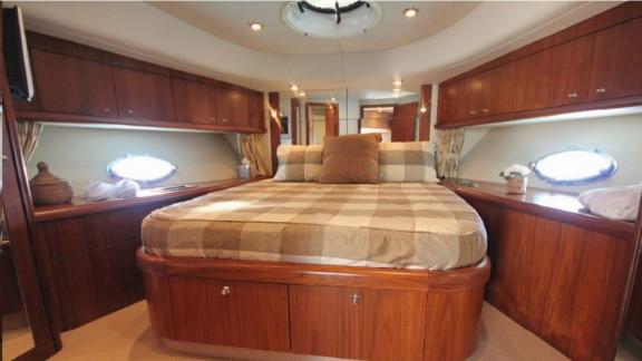 The guest cabin of the Distraction motor yacht features a large bed and stylish wooden details.