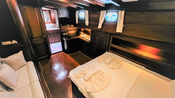 A comfortable ship's cabin with a double bed, sofa and wooden furniture. Windows offer a view of the sea.