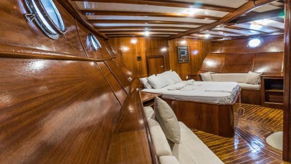 Master cabin with wooden walls, a large bed, and cozy seating areas on the Gulet Optimist in Bodrum.