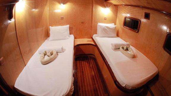 Cabin on Gulet Nirvana 2 with two single beds, wooden walls, small windows, and towels on the beds.