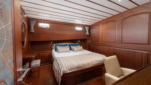 Comfortable bedroom on a boat with double bed, desk and wooden interior.