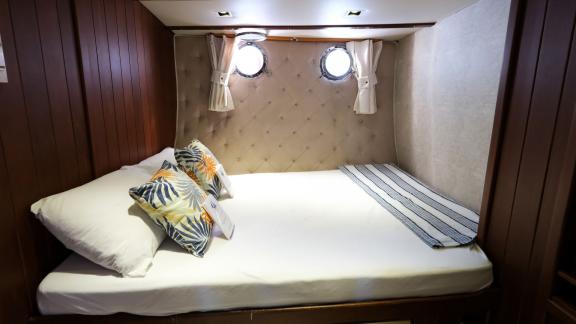 Compact cabin with double bed, tropical pillows, and porthole windows on Gulet Pronto Blue in Fethiye.