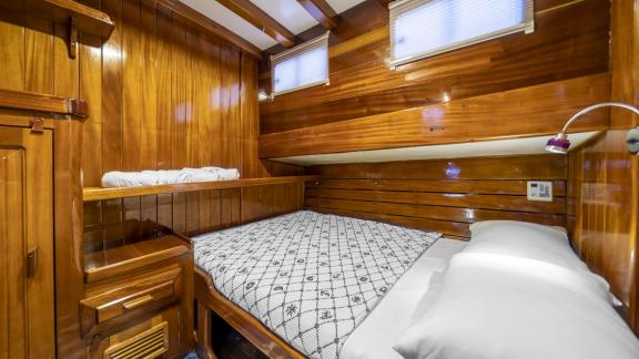 The cabin features a double bed, wooden walls, two windows, and practical storage.