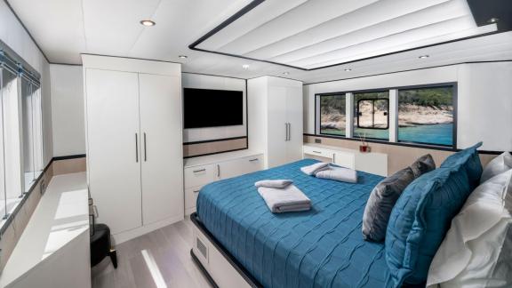 Modern yacht bedroom with panoramic view; equipped with a large bed, TV, and wardrobes for a comfortable space.
