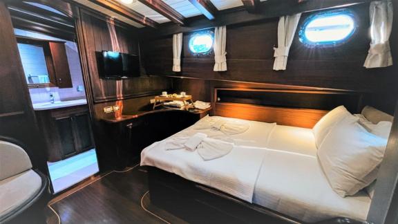 A luxurious ship's cabin with a cosy double bed, TV and adjoining bathroom. Windows offer a sea view.