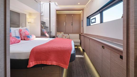 Stylish cabin on the catamaran with a double bed, coral blanket, and separate seating area.