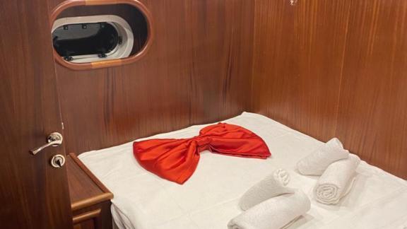 Cabin with a double bed, decorated with a red ribbon and white towels.