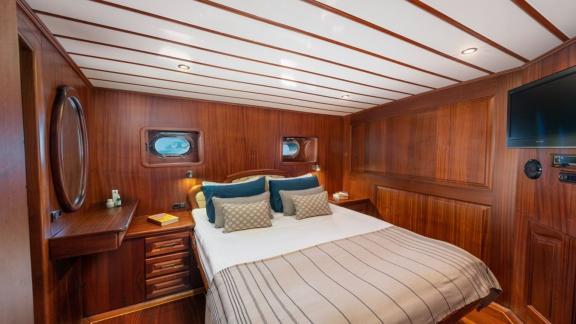 Cosy bedroom on a boat with double bed, wooden interior and TV.