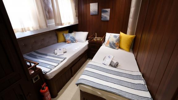 Stylish cabin with two single beds, colorful pillows, and wooden walls on Gulet Pronto Blue in Fethiye.